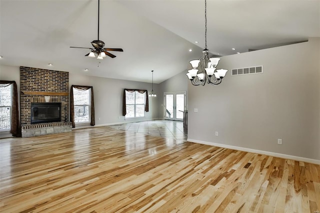 unfurnished living room with ceiling fan with notable chandelier, high vaulted ceiling, a brick fireplace, and light hardwood / wood-style flooring