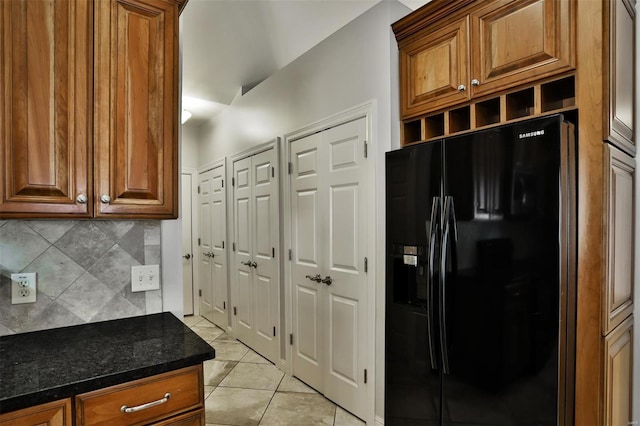 kitchen with dark stone counters, black fridge with ice dispenser, light tile patterned floors, and backsplash