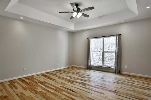 spare room with ceiling fan, light hardwood / wood-style floors, and a tray ceiling