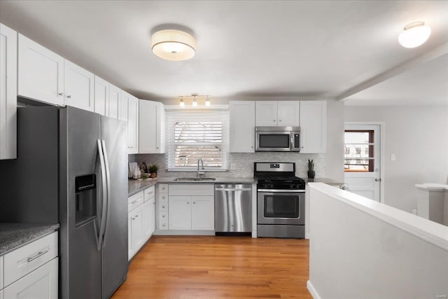 kitchen with sink, appliances with stainless steel finishes, white cabinetry, tasteful backsplash, and light wood-type flooring