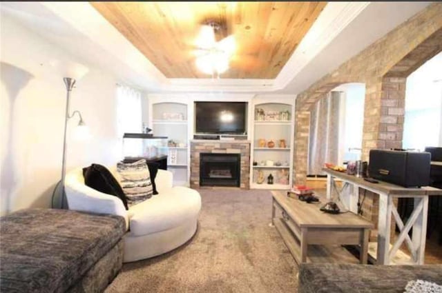 living room featuring a tray ceiling, wood ceiling, built in shelves, and a stone fireplace