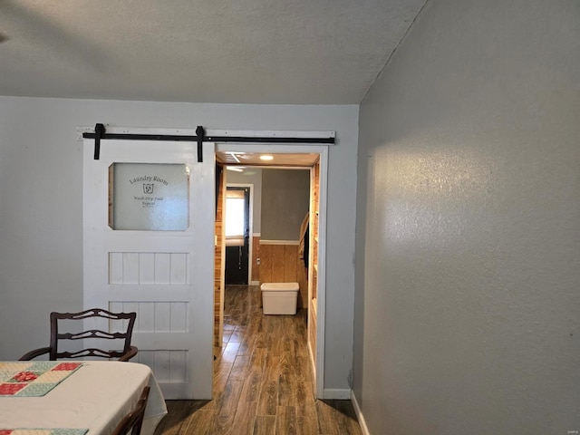 corridor featuring a barn door, dark hardwood / wood-style flooring, and a textured ceiling