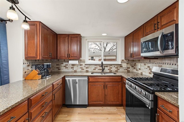 kitchen featuring sink, stainless steel appliances, light hardwood / wood-style floors, light stone countertops, and decorative light fixtures