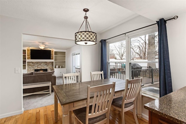 dining room featuring ceiling fan, a fireplace, wood-type flooring, a textured ceiling, and built in shelves