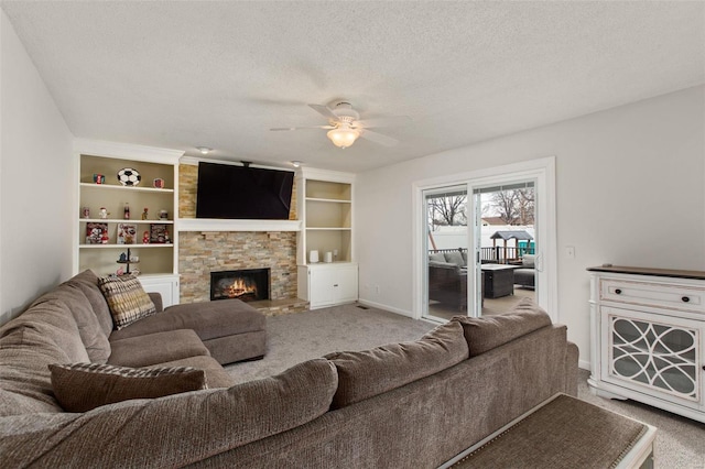 living room with a stone fireplace, carpet flooring, ceiling fan, a textured ceiling, and built in shelves