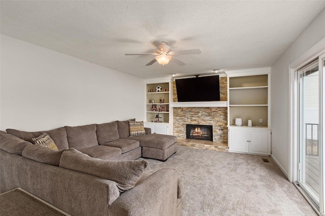 carpeted living room with ceiling fan, a stone fireplace, a textured ceiling, and built in features