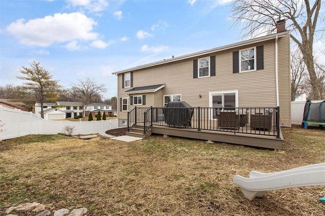 rear view of house with a trampoline, a wooden deck, and a yard