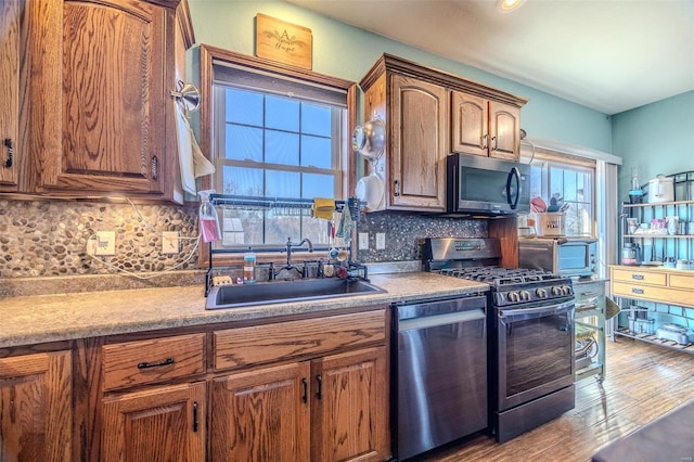 kitchen with tasteful backsplash, sink, light wood-type flooring, and appliances with stainless steel finishes