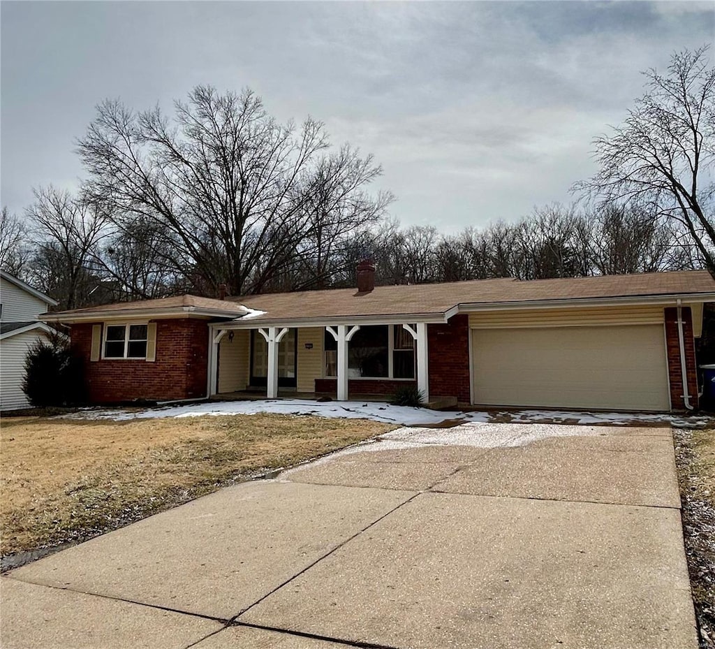 view of front of house featuring a garage, driveway, brick siding, and a chimney