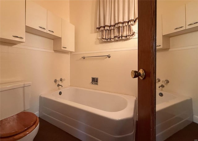 bathroom with a tub to relax in and toilet