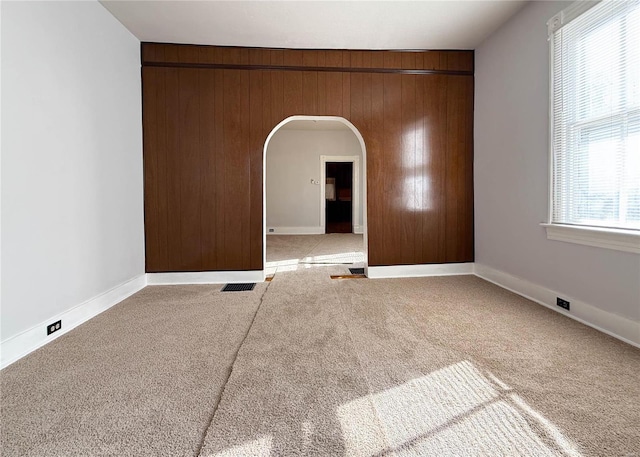 carpeted spare room featuring wood walls