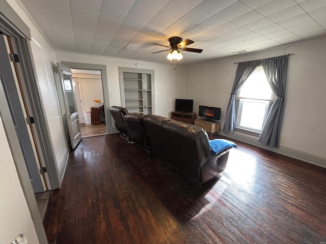 living room with built in shelves, ceiling fan, and dark hardwood / wood-style flooring