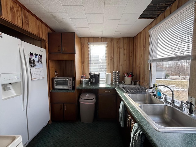 kitchen with sink, white refrigerator with ice dispenser, wooden walls, and plenty of natural light