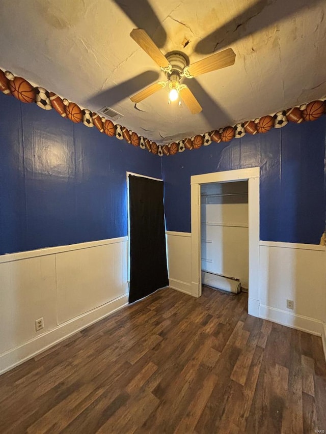 empty room with a baseboard heating unit, dark wood-type flooring, and ceiling fan