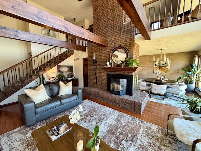 living room featuring a towering ceiling, a wood stove, a chandelier, hardwood / wood-style flooring, and beam ceiling