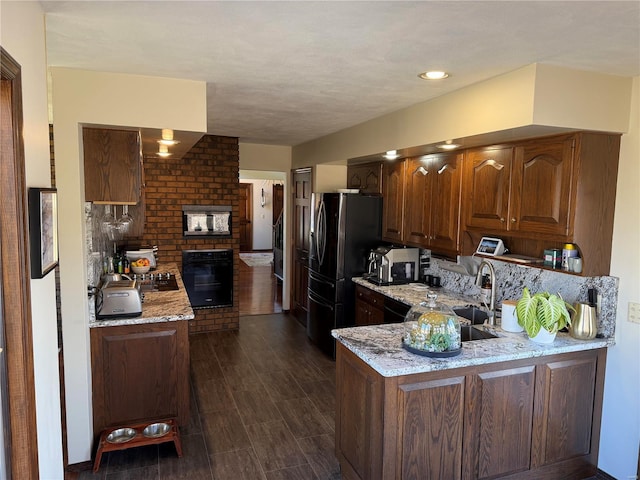 kitchen with black refrigerator, a brick fireplace, light stone counters, and kitchen peninsula