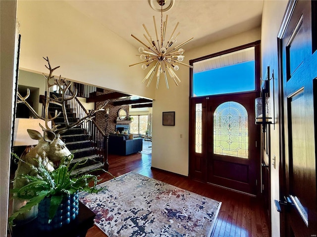 entrance foyer featuring a brick fireplace, dark hardwood / wood-style floors, a notable chandelier, and a towering ceiling