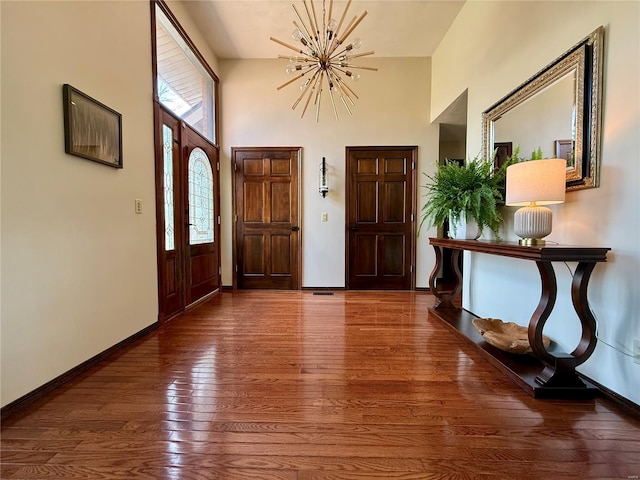 entryway with baseboards, a towering ceiling, hardwood / wood-style flooring, and an inviting chandelier