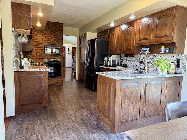 kitchen with freestanding refrigerator, a peninsula, light stone counters, black oven, and built in microwave