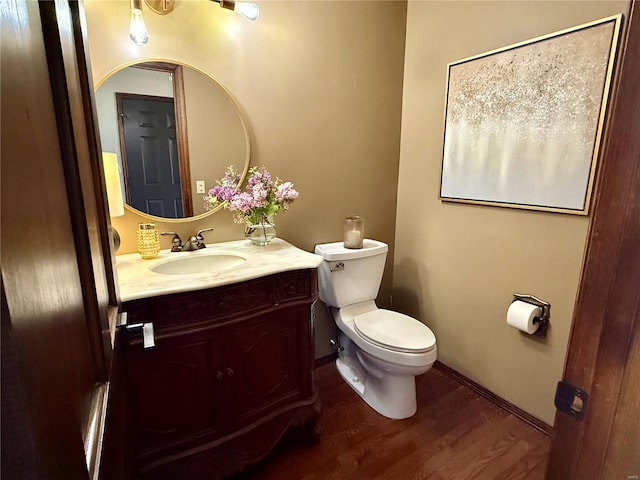half bathroom with vanity, baseboards, toilet, and wood finished floors