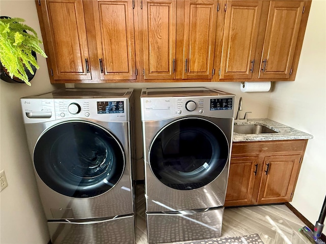 clothes washing area with washer and dryer, light wood-type flooring, a sink, and cabinet space