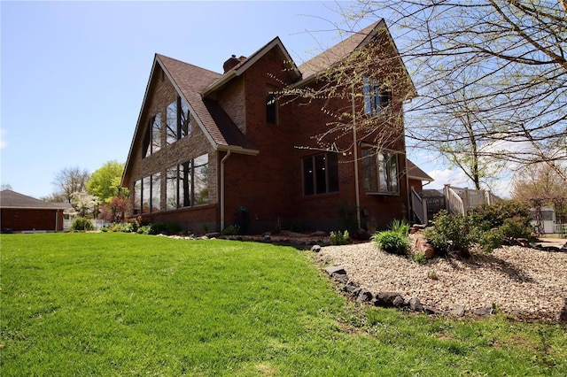 view of side of home with brick siding, roof with shingles, a lawn, and a chimney