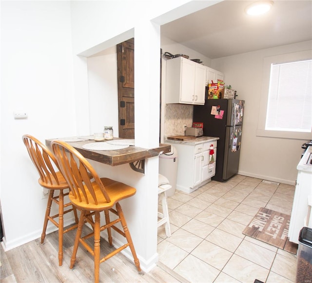 kitchen with decorative backsplash, a kitchen breakfast bar, stainless steel refrigerator, and white cabinets