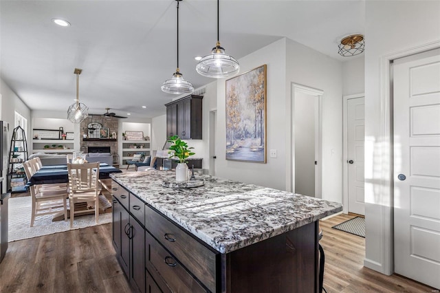 kitchen featuring dark brown cabinetry, built in shelves, a stone fireplace, and wood-type flooring