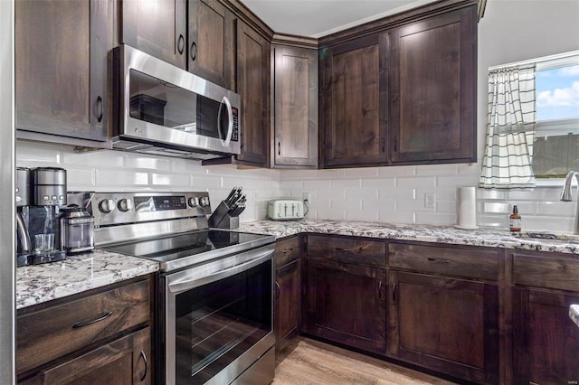 kitchen featuring stainless steel appliances, dark brown cabinets, light stone counters, and light wood-type flooring