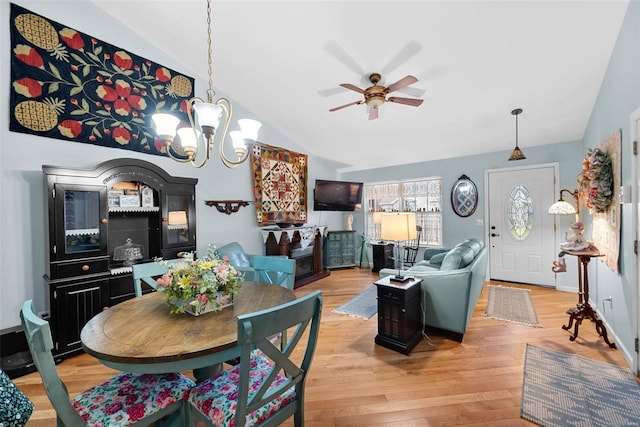 dining space with vaulted ceiling, ceiling fan with notable chandelier, and light hardwood / wood-style flooring