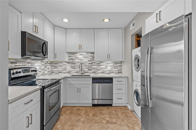 kitchen with stacked washer and clothes dryer, sink, white cabinetry, stainless steel appliances, and backsplash