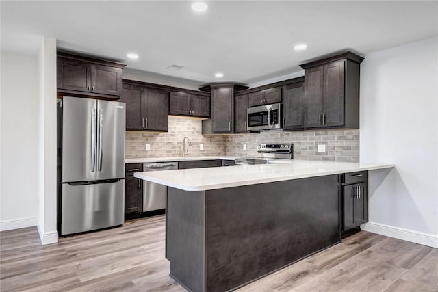 kitchen featuring appliances with stainless steel finishes, kitchen peninsula, dark brown cabinets, and light hardwood / wood-style flooring