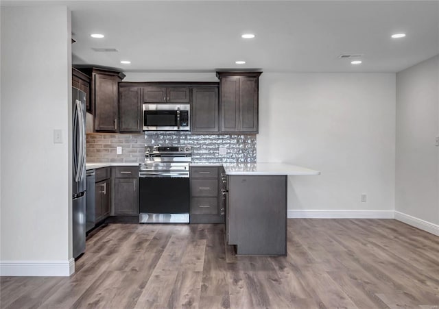 kitchen with stainless steel appliances, wood-type flooring, dark brown cabinets, and decorative backsplash