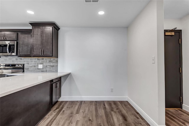 kitchen with tasteful backsplash, dark brown cabinetry, appliances with stainless steel finishes, and light hardwood / wood-style flooring