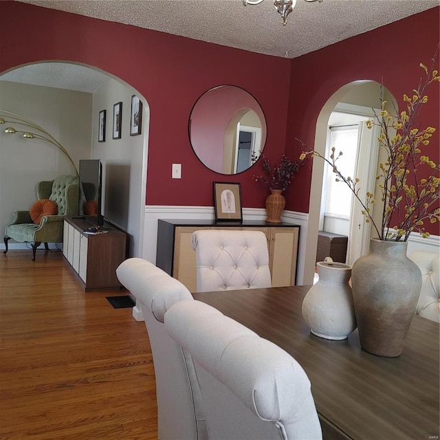 dining space with wainscoting, a textured ceiling, and wood finished floors