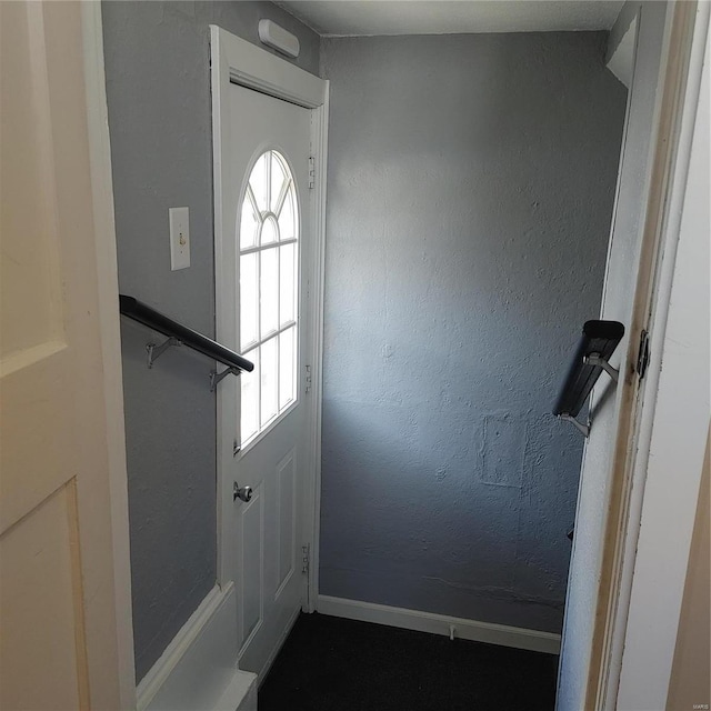 doorway featuring a textured wall and baseboards