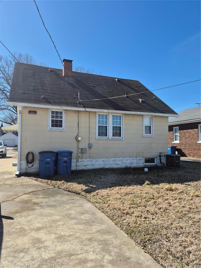 rear view of house with a shingled roof, a chimney, and central AC unit