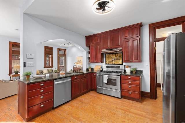 kitchen featuring sink, dark stone countertops, kitchen peninsula, stainless steel appliances, and light hardwood / wood-style floors