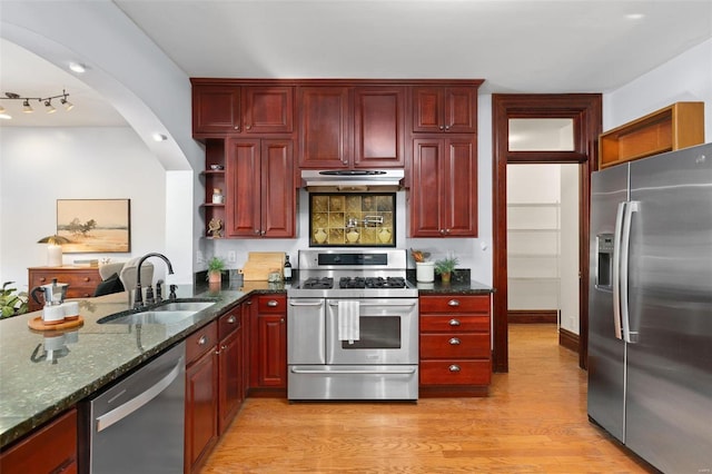 kitchen featuring appliances with stainless steel finishes, sink, dark stone countertops, and light hardwood / wood-style flooring