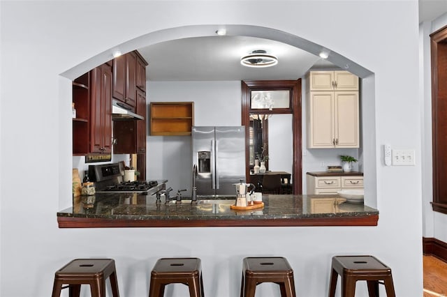 kitchen featuring sink, dark stone countertops, kitchen peninsula, stainless steel appliances, and cream cabinetry