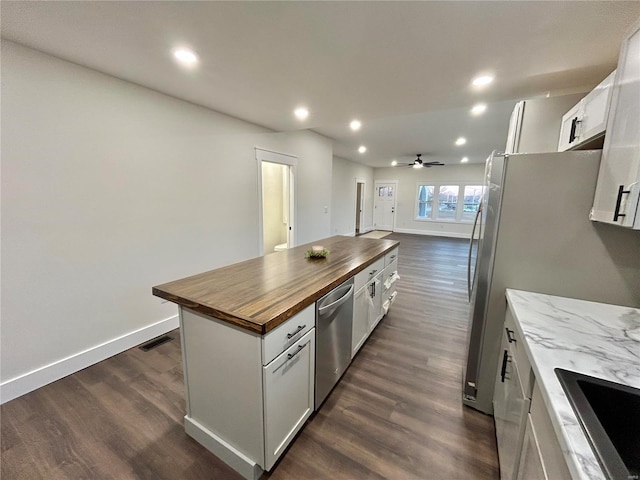 kitchen featuring dark wood-type flooring, appliances with stainless steel finishes, a center island, white cabinets, and wood counters