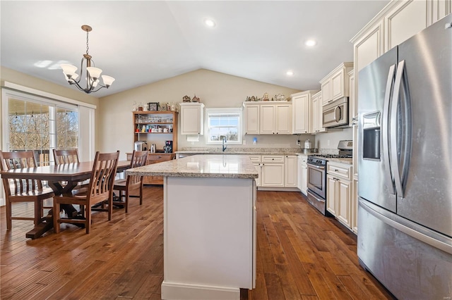 kitchen with dark wood-type flooring, stainless steel appliances, light stone counters, a kitchen island, and decorative light fixtures