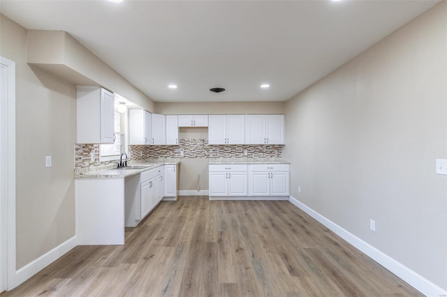 kitchen featuring sink, light stone countertops, light hardwood / wood-style floors, decorative backsplash, and white cabinets