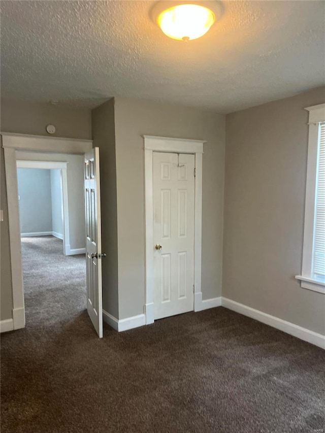 unfurnished bedroom with a textured ceiling, dark carpet, and a closet