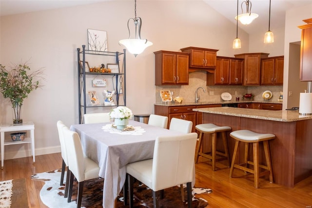 dining area with wood-type flooring, sink, and high vaulted ceiling