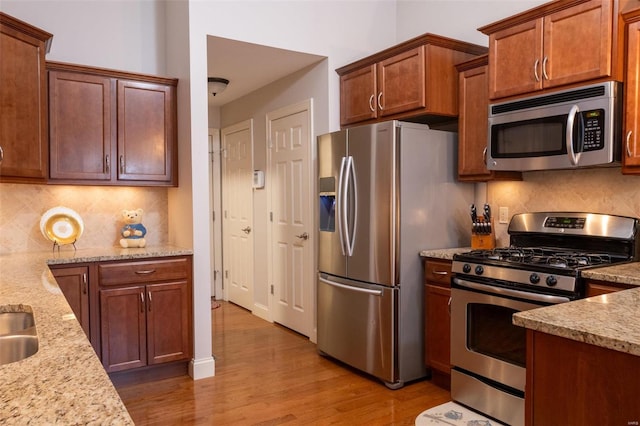 kitchen featuring light stone counters, appliances with stainless steel finishes, backsplash, and light wood-type flooring