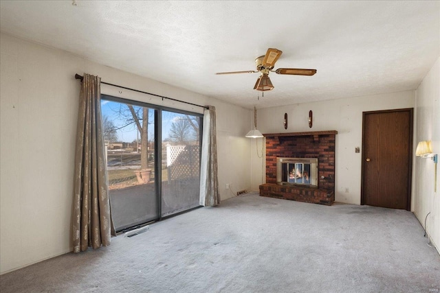 unfurnished living room featuring a brick fireplace, a textured ceiling, carpet floors, and ceiling fan