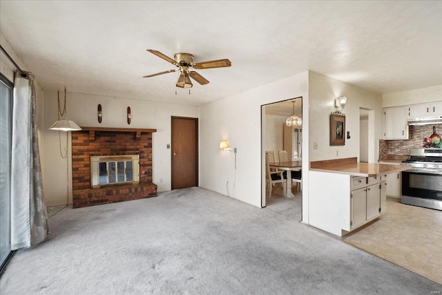 kitchen with white cabinetry, backsplash, light colored carpet, a brick fireplace, and stainless steel gas range