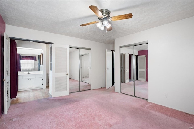 unfurnished bedroom featuring sink, ensuite bath, light carpet, a textured ceiling, and multiple closets