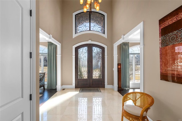 entryway with baseboards, french doors, a high ceiling, and an inviting chandelier